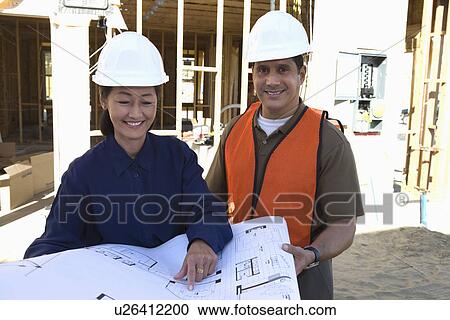 Stock Image - Architect and construction worker looking at blueprints on construction site. Fotosearch