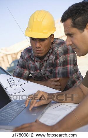 Stock Image - Architect and construction worker using laptop on construction site. Fotosearch