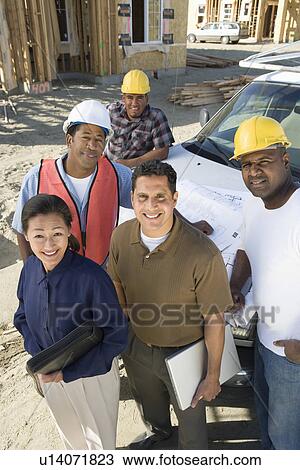 Stock Image - Architect and four construction workers standing in front of car on construction site. Fotosearch