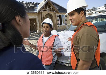 Stock Image - Architect and two construction workers having discussion on construction site. Fotosearch