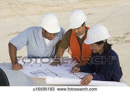 Stock Image - Architect and two construction workers looking at blueprints on construction site. Fotosearch