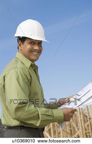 Architect holding blueprints on construction site View Large Photo Image Stock Image - Architect holding blueprints on construction site. Fotosearch