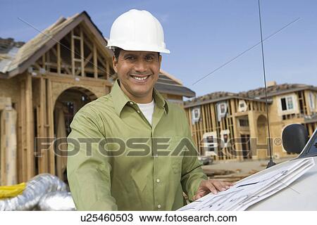 Stock Image - Architect holding blueprints on construction site. Fotosearch