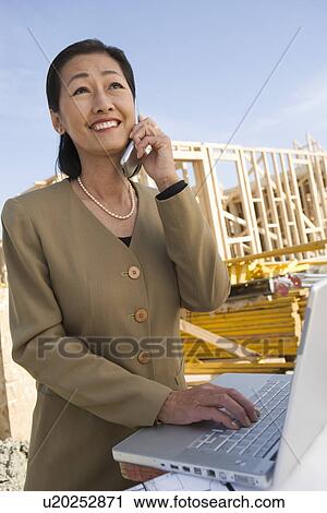 Stock Image - Architect talking on mobile phone and using laptop. Fotosearch