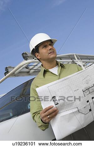 Stock Image - Architect talking on mobile phone holding blueprints. Fotosearch