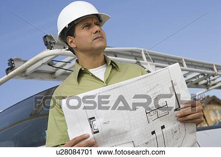 Stock Image - Architect talking on mobile phone holding blueprints. Fotosearch