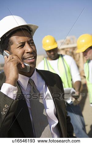 Architect using mobile phone and two construction works looking at blueprints View Large Photo Image Stock Image - Architect using mobile phone and two construction works looking at blueprints. Fotosearch