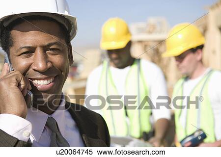 Architect using mobile phone and two construction works looking at blueprints View Large Photo Image Stock Photography - Architect using mobile phone and two construction works looking at blueprints. Fotosearch