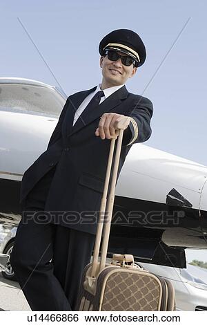 Asian male pilot leaning at suitcase in front of airplane, elevated view. View Large Photo Image Stock Photograph - Asian male pilot leaning at suitcase in front of airplane, elevated view.. Fotosearch