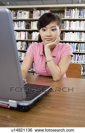 Stock Photograph - Bored female student working on laptop in library. Fotosearch