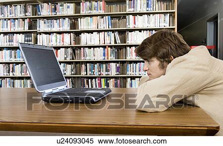 Stock Photography - Bored male student with laptop at library. Fotosearch