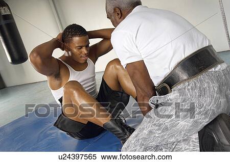 Stock Photography - Boxer doing sit-ups with coach in gym. Fotosearch