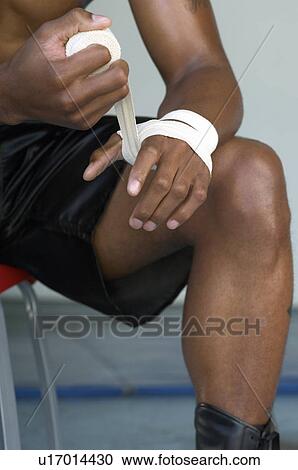 Stock Image - Boxer wrapping hands in tape, close up, mid section. Fotosearch