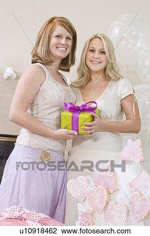 Stock Image - Bride and Friend standing Together holding gift at Bridal Shower. Fotosearch