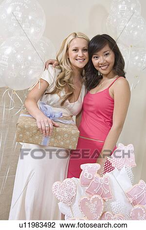 Stock Image - Bride and Friend standing Together holding gift at Bridal Shower. Fotosearch