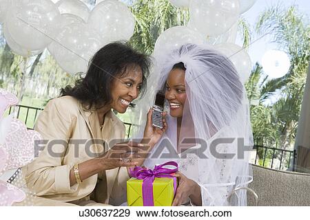 Bride using mobile phone with mother at bridal shower View Large Photo Image Stock Photo - Bride using mobile phone with mother at bridal shower. Fotosearch