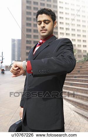 Stock Photograph - Business man checking watch on city street. Fotosearch