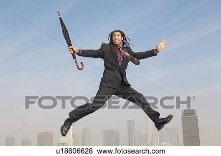 Stock Photo - Business man jumping with closed umbrella mid-air above city. Fotosearch