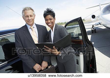 Stock Photo - Businesspeople standing in door of car on landing strip near private jet. Fotosearch