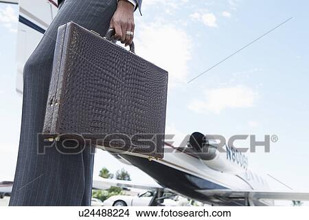 Picture - Businesswoman Holding a Briefcase outside of airplane, low section. Fotosearch