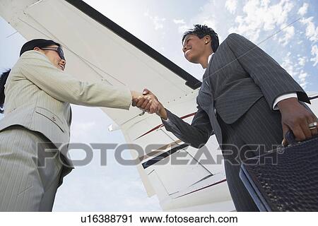 Businesswomen Shaking Hands below airplane wing, low angle view View Large Photo Image Stock Image - Businesswomen Shaking Hands below airplane wing, low angle view. Fotosearch