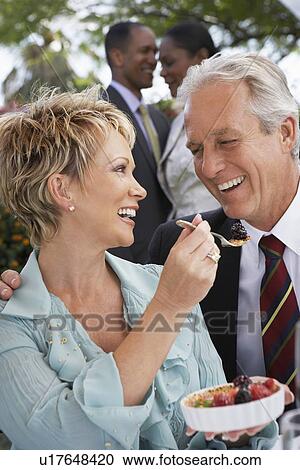 Stock Image - Cheerful elegant couple sharing dessert together at garden party. Fotosearch