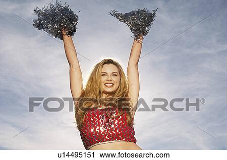 Stock Image - Cheerleader with pom poms raised, portrait. Fotosearch