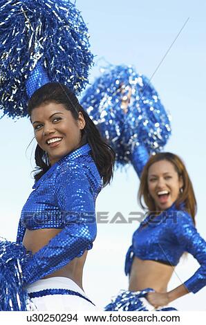 Picture - Cheerleaders with pom poms raised looking over shoulder. Fotosearch
