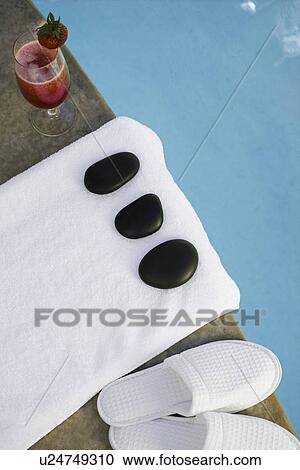 Stock Image - Cocktail beside stones, towel and slippers at health spa. Fotosearch