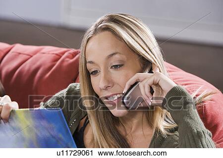 Stock Image - College girl student on couch, telephoning while reading. Fotosearch