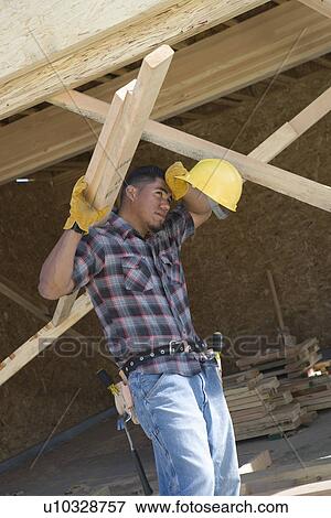 Stock Photo - Construction worker carrying planks and wiping his forehead on construction site. Fotosearch