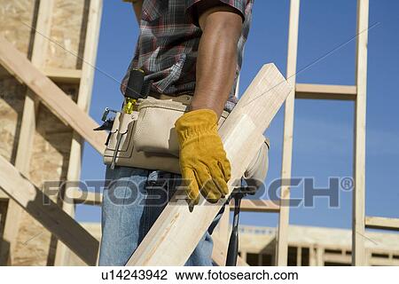 Construction worker carrying planks on construction site View Large Photo Image Stock Image - Construction worker carrying planks on construction site. Fotosearch
