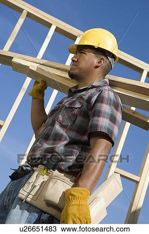 Construction worker carrying planks on construction site View Large Photo Image Stock Image - Construction worker carrying planks on construction site. Fotosearch
