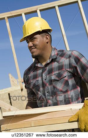 Construction worker carrying planks on construction site View Large Photo Image Stock Photo - Construction worker carrying planks on construction site. Fotosearch
