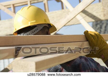 Stock Photo - Construction worker carrying planks on construction site. Fotosearch
