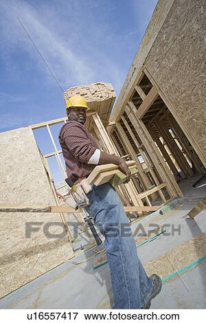 Stock Photo - Construction worker carrying wooden plank. Fotosearch