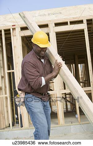 Stock Photograph - Construction worker carrying wooden plank. Fotosearch