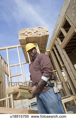 Stock Photography - Construction worker carrying wooden plank. Fotosearch