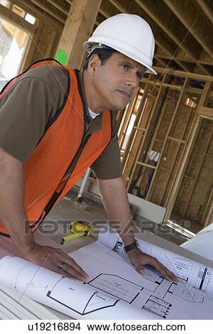 Picture - Construction worker examining blueprints inside half constructed house. Fotosearch