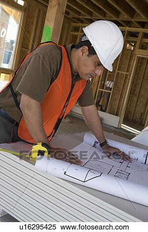 Stock Photography - Construction worker examining blueprints inside half constructed house. Fotosearch