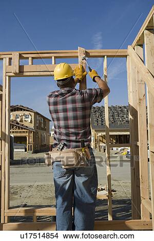 Construction worker hammering nail on construction site View Large Photo Image Picture - Construction worker hammering nail on construction site. Fotosearch