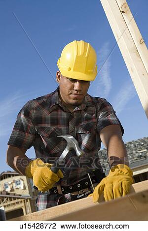 Construction worker hammering nail on construction site View Large Photo Image Stock Image - Construction worker hammering nail on construction site. Fotosearch
