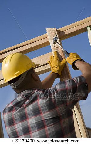 Construction worker hammering nail on construction site View Large Photo Image Stock Image - Construction worker hammering nail on construction site. Fotosearch