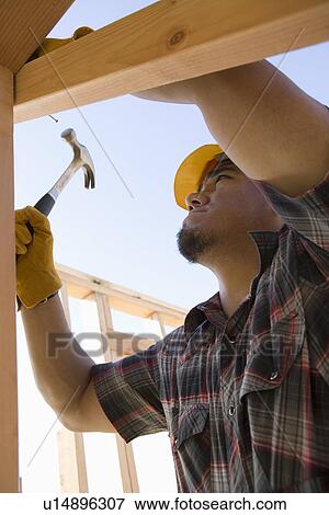 Construction worker hammering nail on construction site View Large Photo Image Stock Photo - Construction worker hammering nail on construction site. Fotosearch