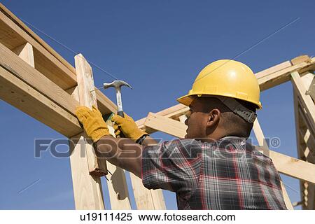 Stock Photography - Construction worker hammering nail on construction site. Fotosearch