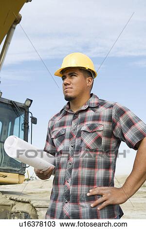 Stock Image - Construction worker holding blueprints on site. Fotosearch