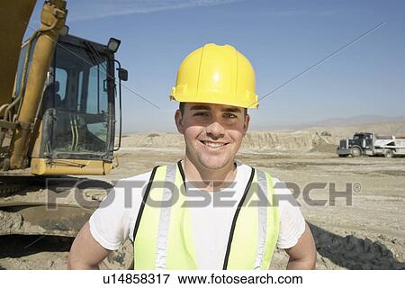 Construction Worker in hard hat standing in front of heavy machinery View Large Photo Image Stock Photo - Construction Worker in hard hat standing in front of heavy machinery. Fotosearch
