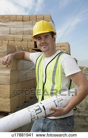 Construction Worker leaning on stack of lumber, holding building plan View Large Photo Image Stock Image - Construction Worker leaning on stack of lumber, holding building plan. Fotosearch