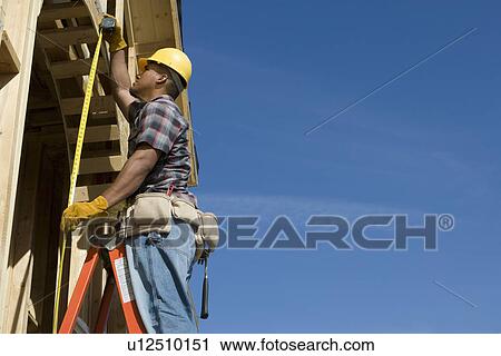 Stock Image - Construction worker measuring half constructed doorway with tape measure. Fotosearch