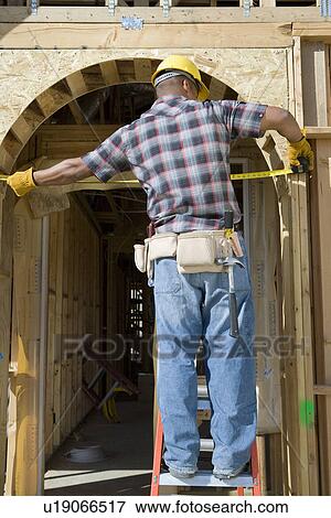Stock Photo - Construction worker measuring half constructed doorway with tape measure. Fotosearch